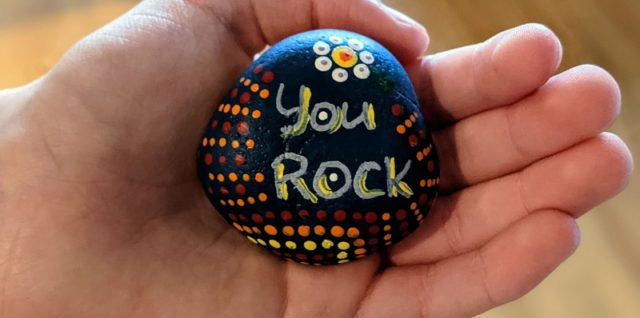 A hand holding a rock with the words "You Rock"