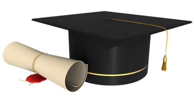 A black graduation cap with gold tassel, resting next to a scrolled diploma