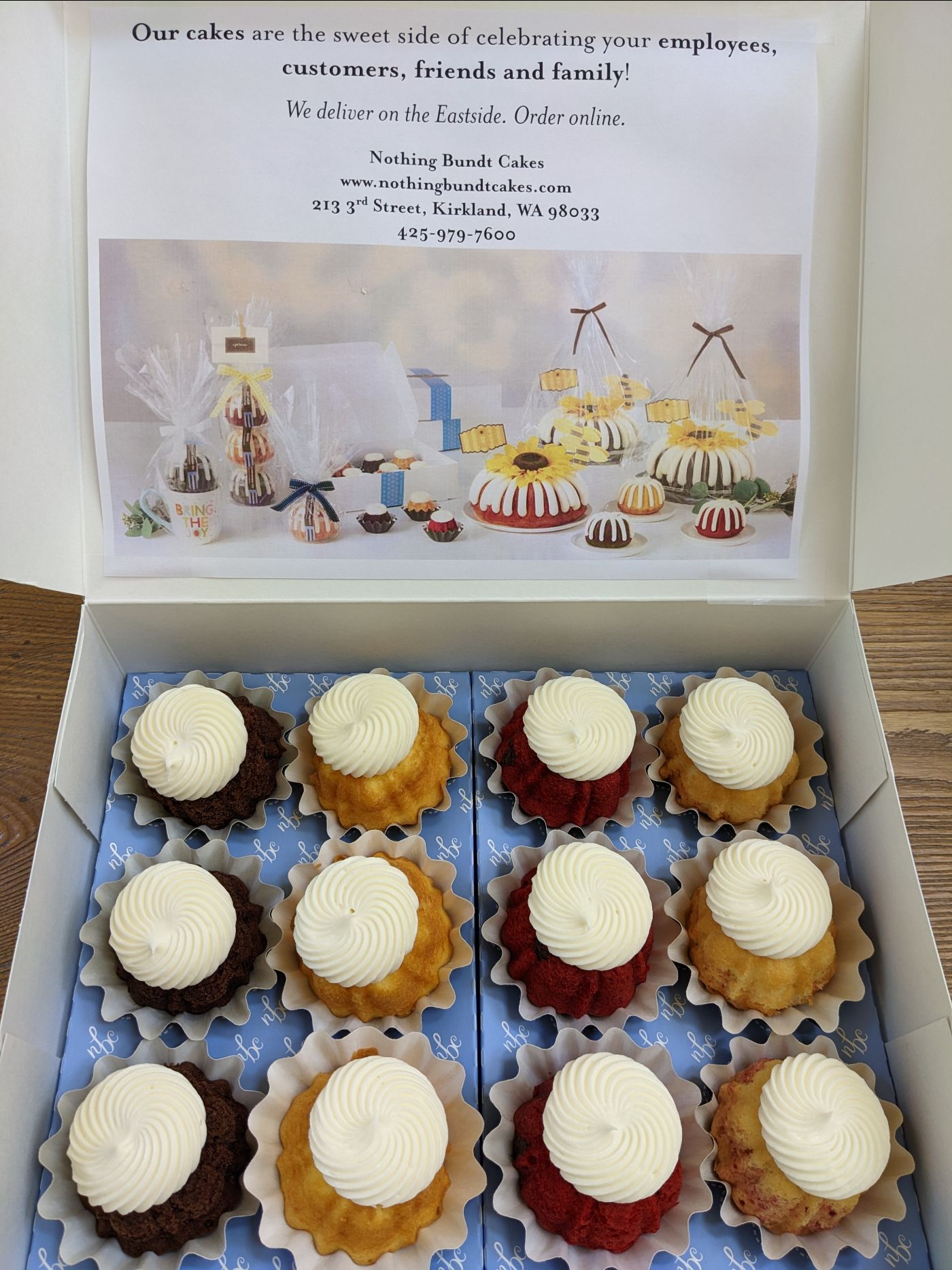 An open box filled with one dozen frosted mini bundt cakes in a variety of flavors